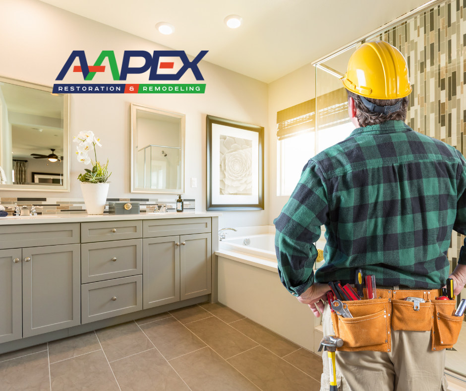 Professional contractor examining a bathroom with his hands on his hips. Aapex logo top left.